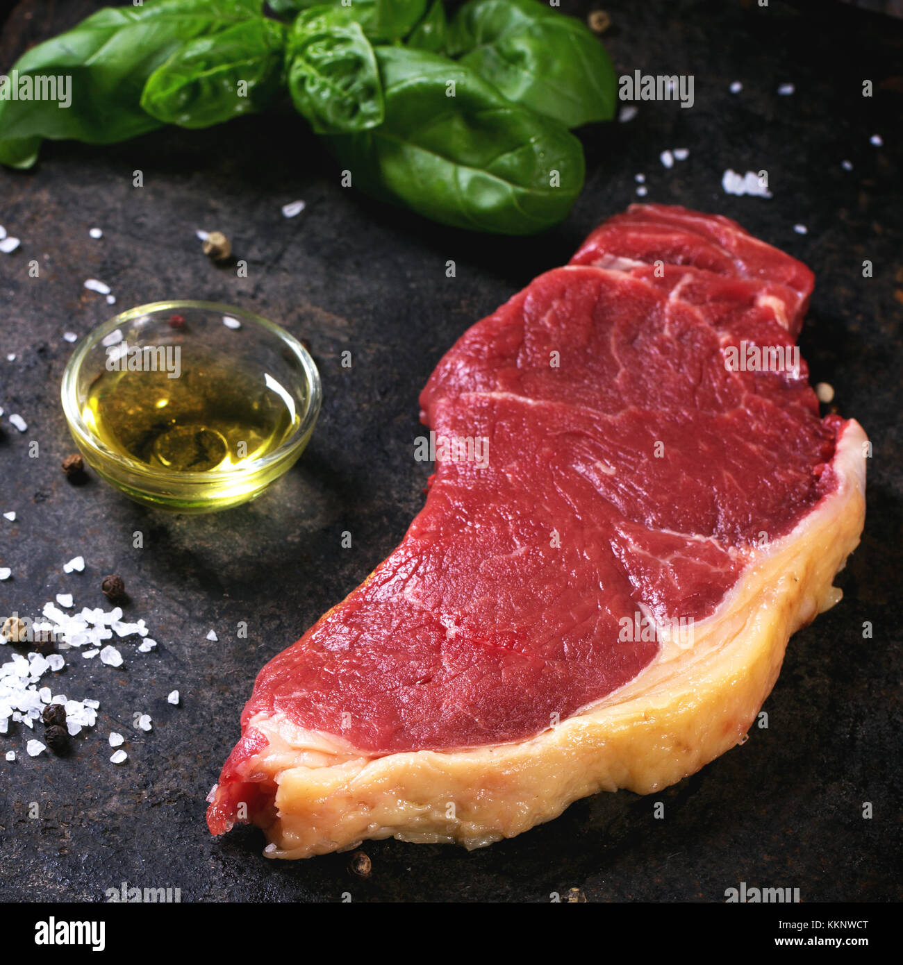 Raw steak with basil and olive oil over black background. Square image