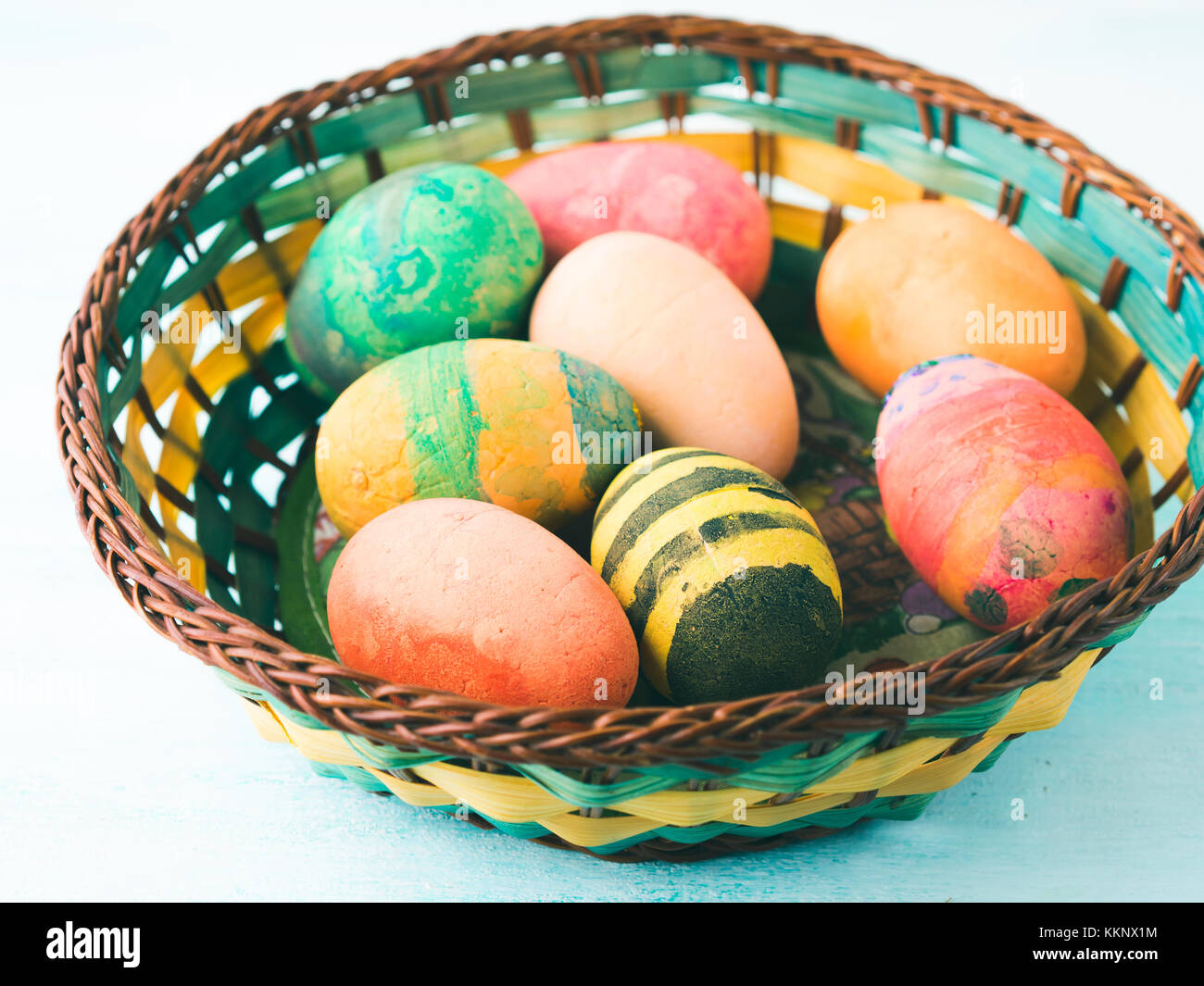 Funny Colorful Easter eggs hand painted by kids in basket on green pastel background Stock Photo
