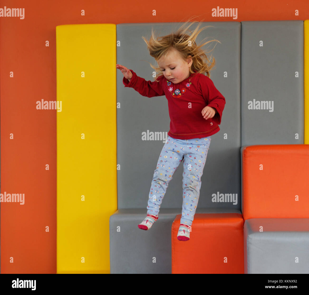 A little girl (3 yrs old) jumping in a padded play area Stock Photo