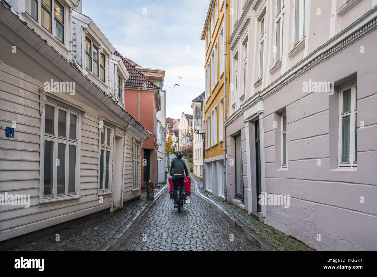 Bergen, Norway -  October 2017 :  Man delivering food on a bicycle on the narrow cobble stoned streets between old white traditional houses in the old Stock Photo