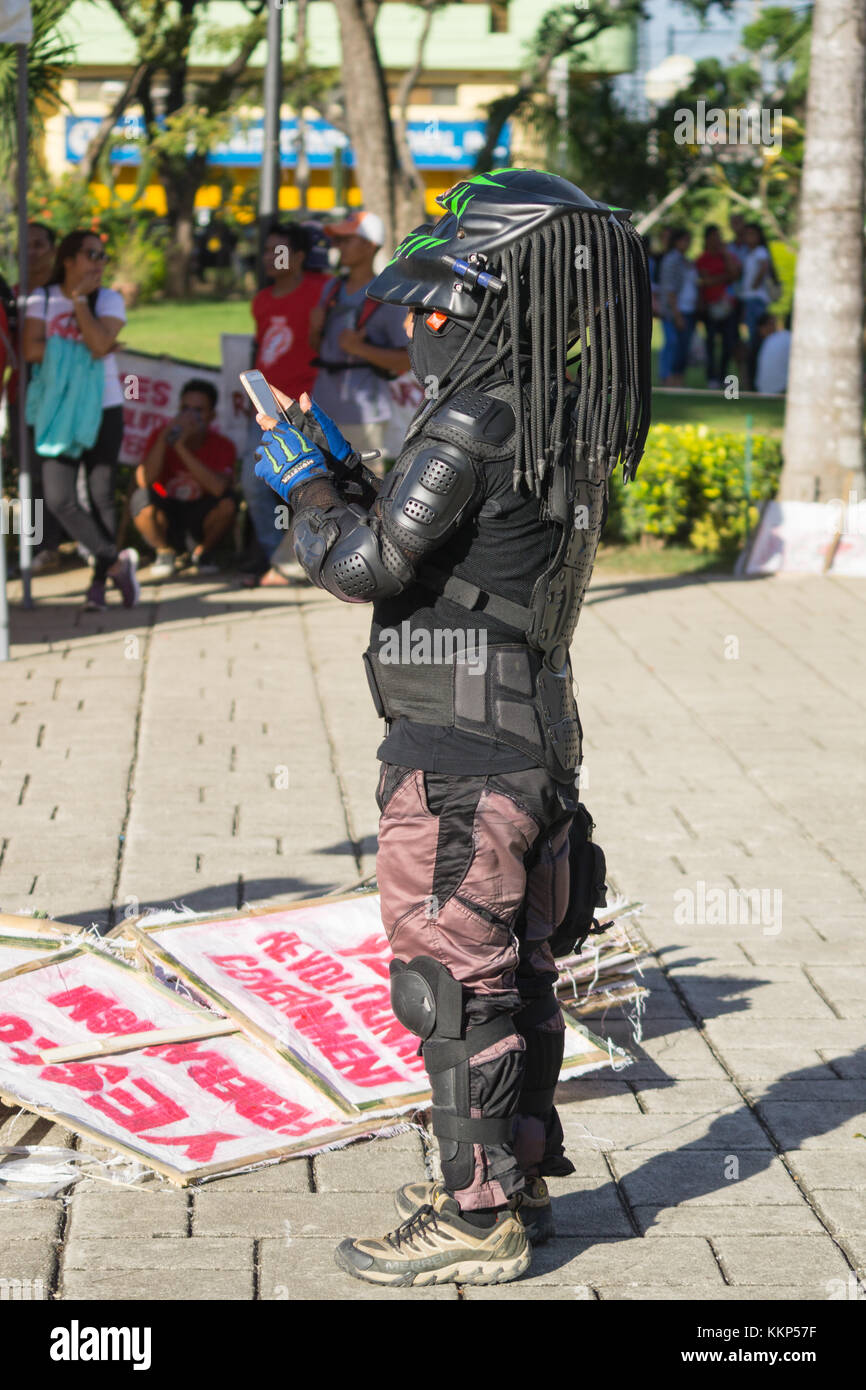 A motorcyclist dressed in Predator headgear taking a photo with a mobile phone,Cebu City,Philippines Stock Photo