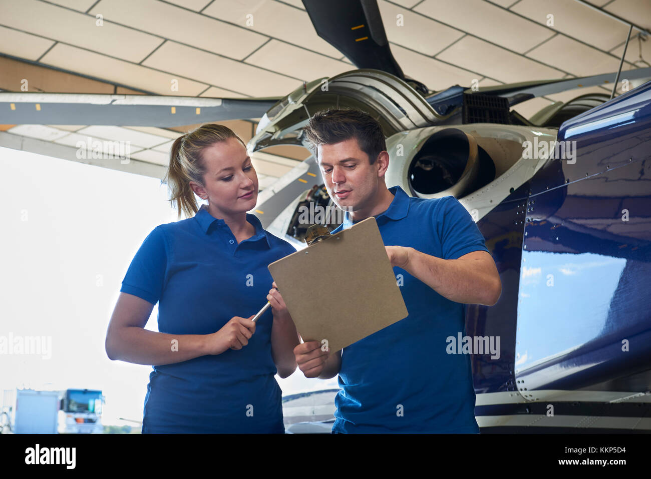 Aero Engineer And Apprentice Working On Helicopter In Hangar Looking At Clipboard Stock Photo