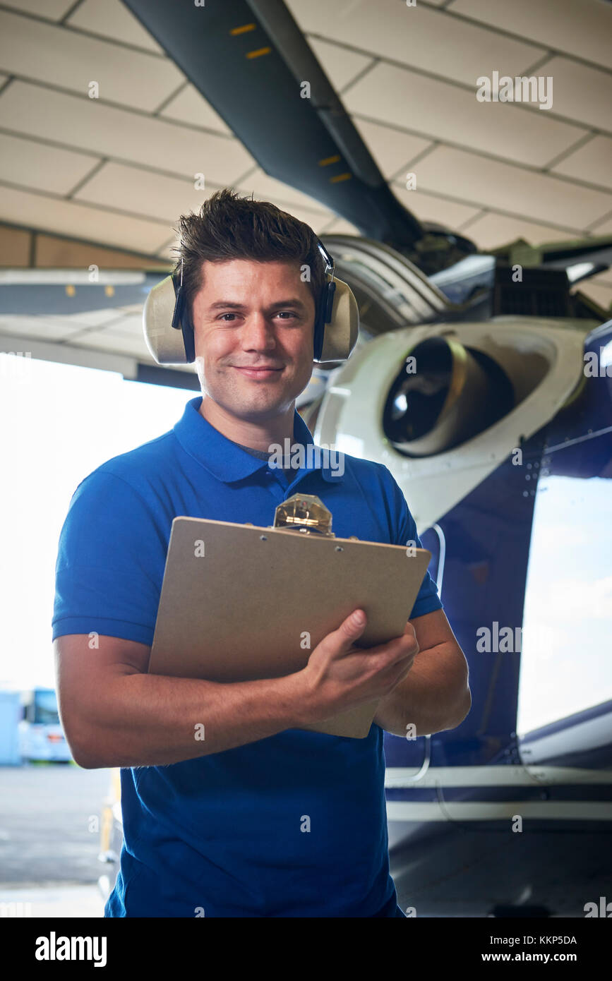 Portrait Of Male Aero Engineer With Clipboard Carrying Out Check On Helicopter In Hangar Stock Photo