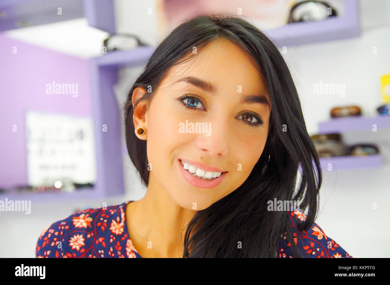 Beautiful young woman wearing a blue contact lense in optical store, in blurred background Stock Photo