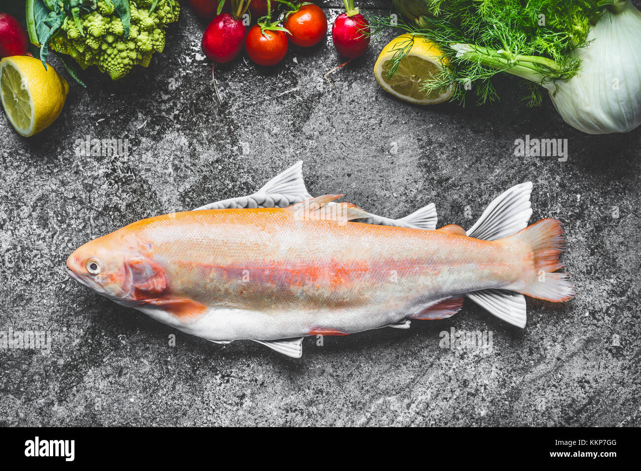Raw fresh whole Gold Rainbow trout in fish dish with vegetables ingredients on gray concrete background , top view.  Healthy Food concept Stock Photo