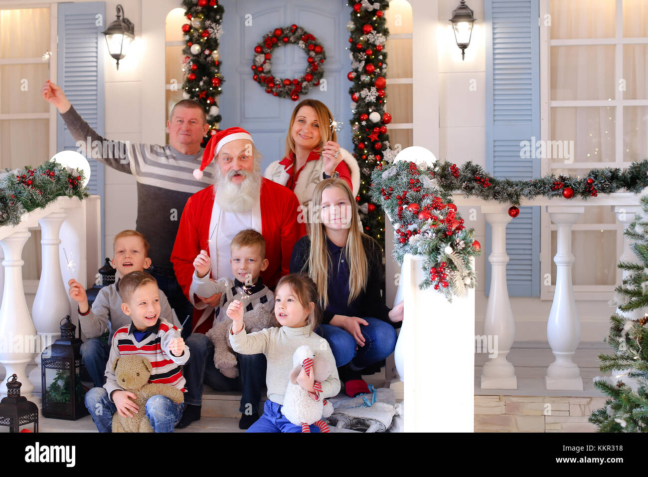 Gladden parents rejoicing with adopted kids singing songs.  Jocund Father Frost smiling with Bengal light. Concept of happiness in adopted family circ Stock Photo