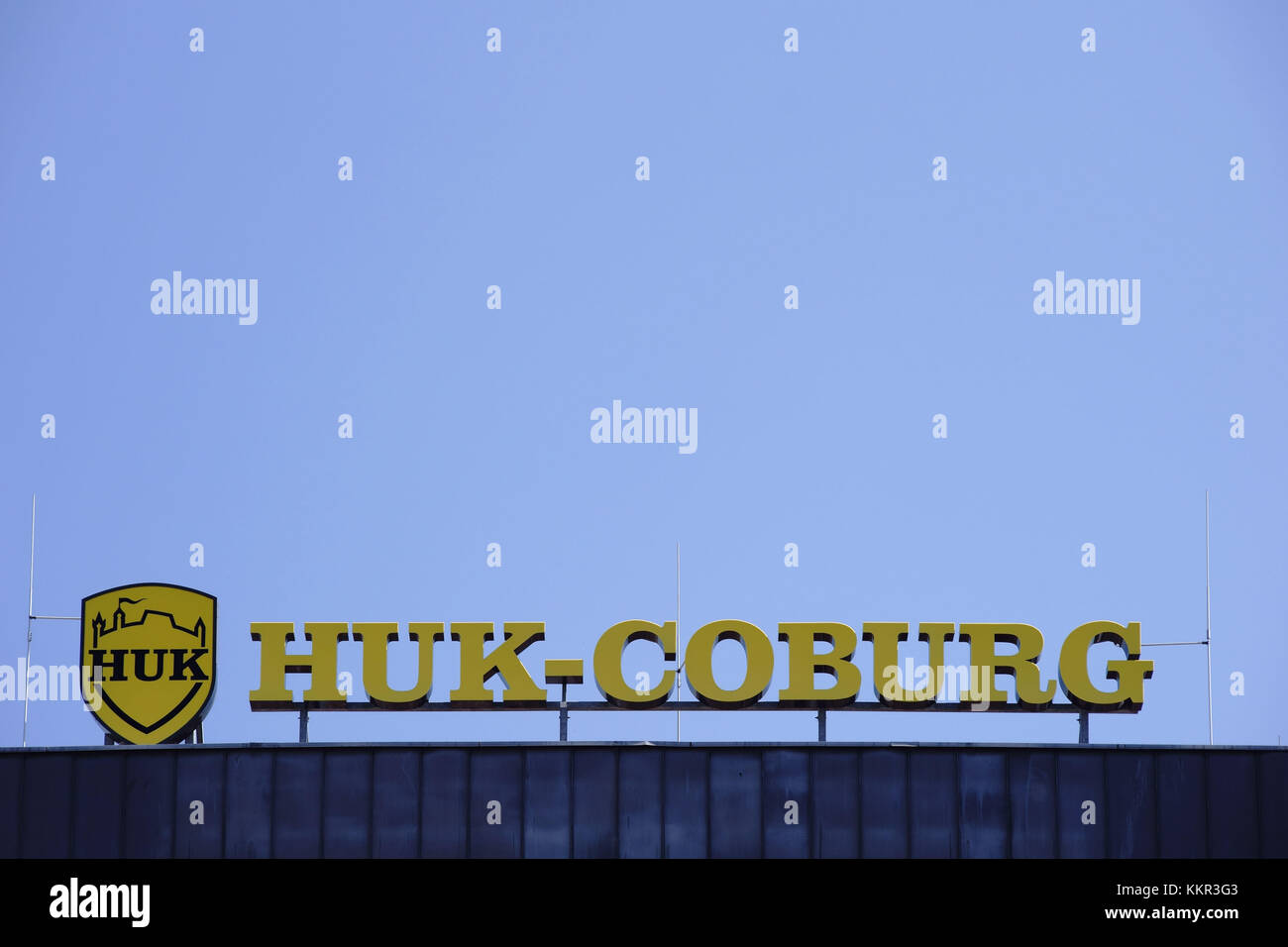The yellow company sign and logo of the insurance company HUK Coburg at the roof edge of an office building in Mainz. Stock Photo