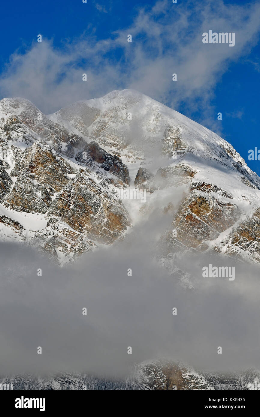 A vertical image of a snow-capped rocky mountain top with swirling white snow and copyspace. Stock Photo