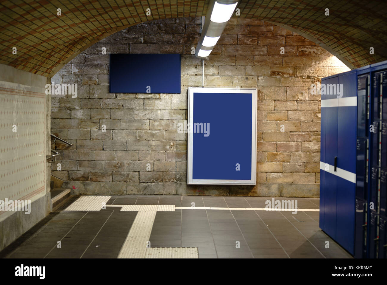 An illuminateded and tiled railway station tunnel with ceiling lamps and frames for advertising poster. Stock Photo