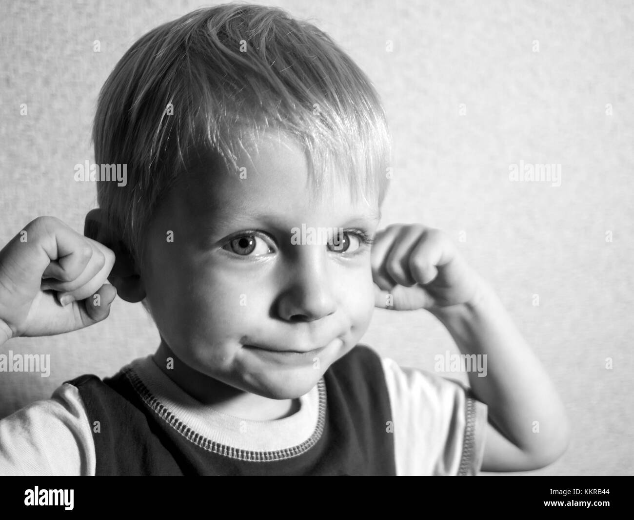 4-year-old Caucasian boy builds fanny face, lifting his fists to his head Stock Photo