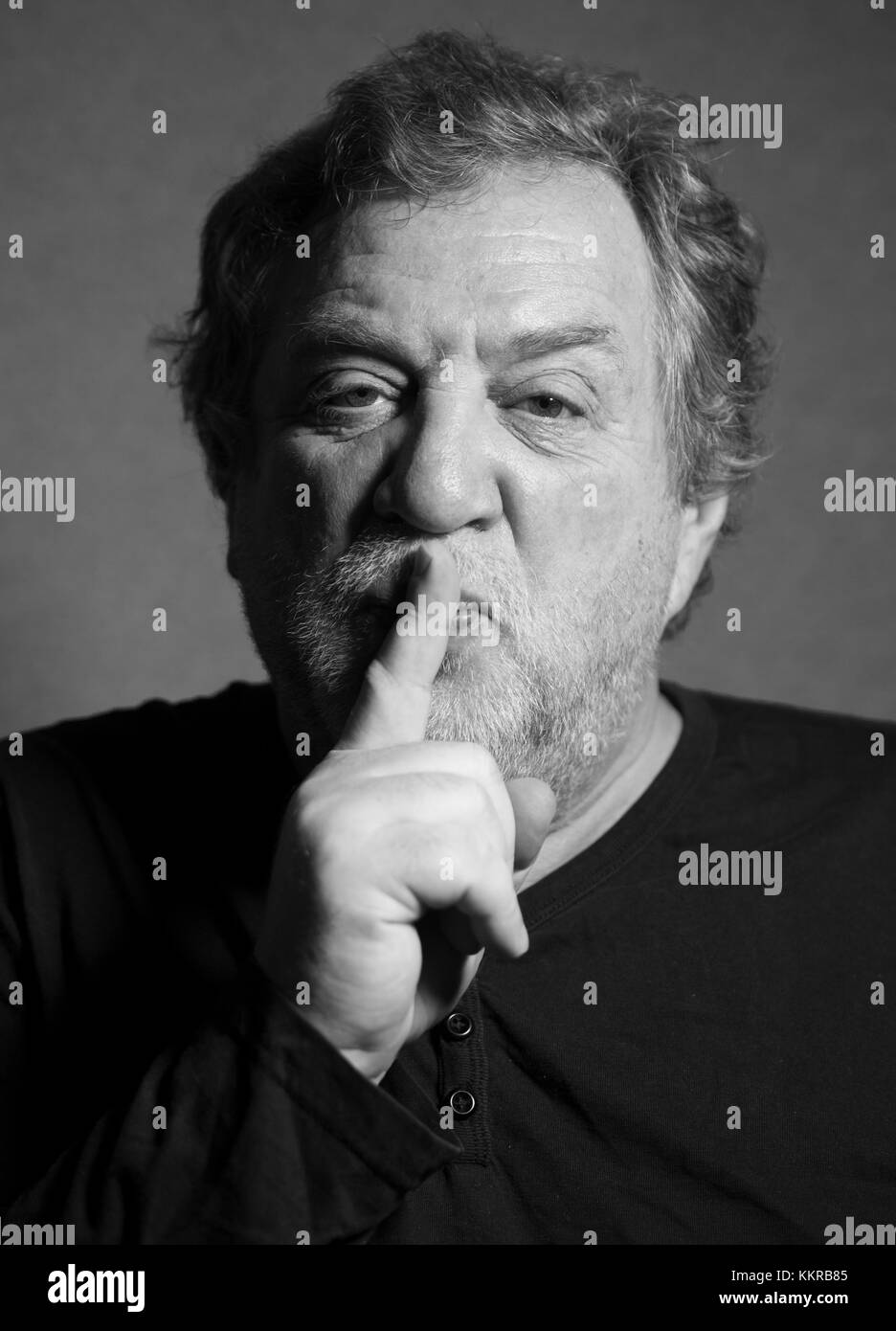 black and white portrait of middle aged caucasian man who put his index finger to his lips, calling for silence Stock Photo