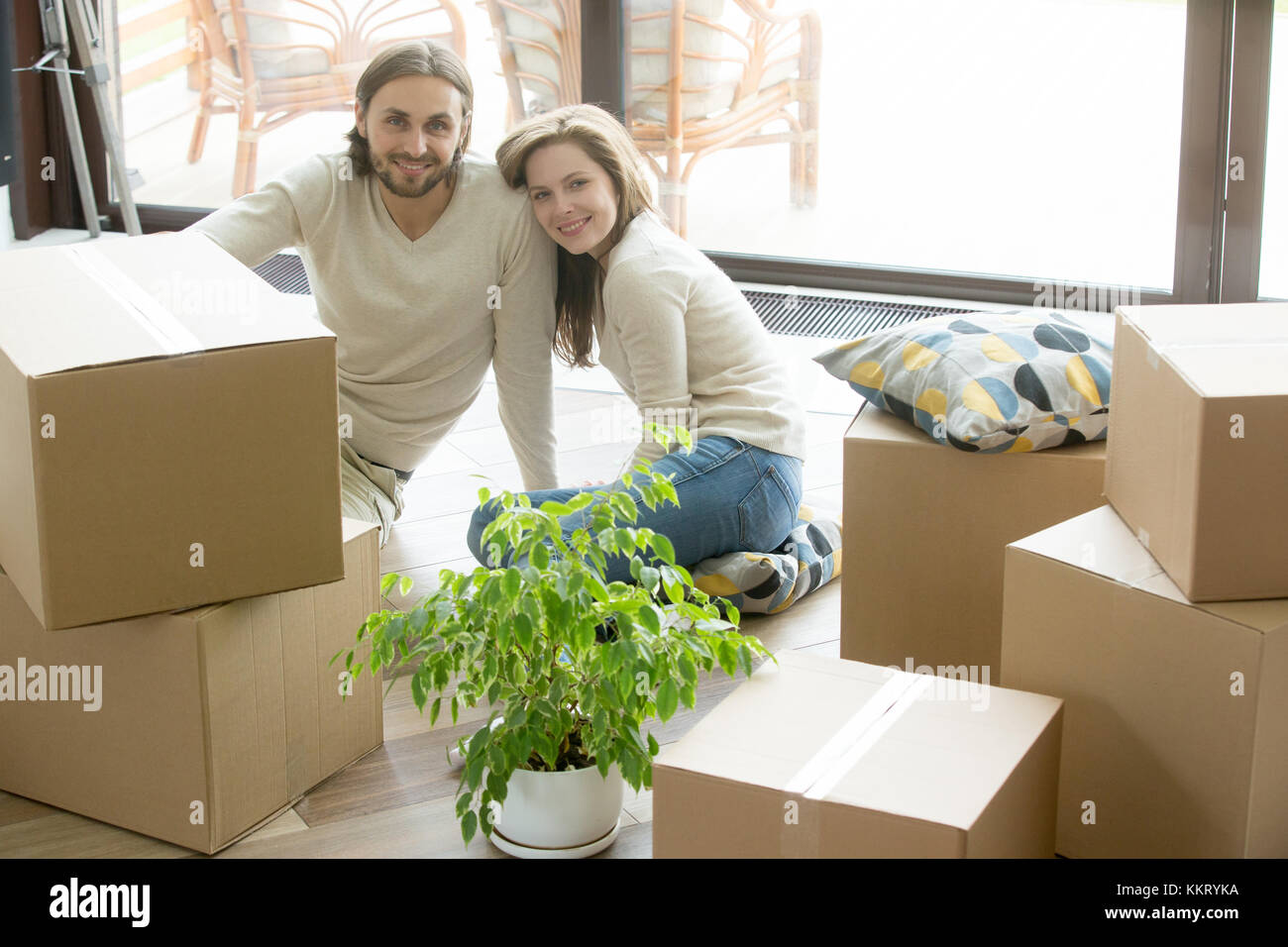 Happy couple looking at camera sitting with boxes, moving day Stock Photo