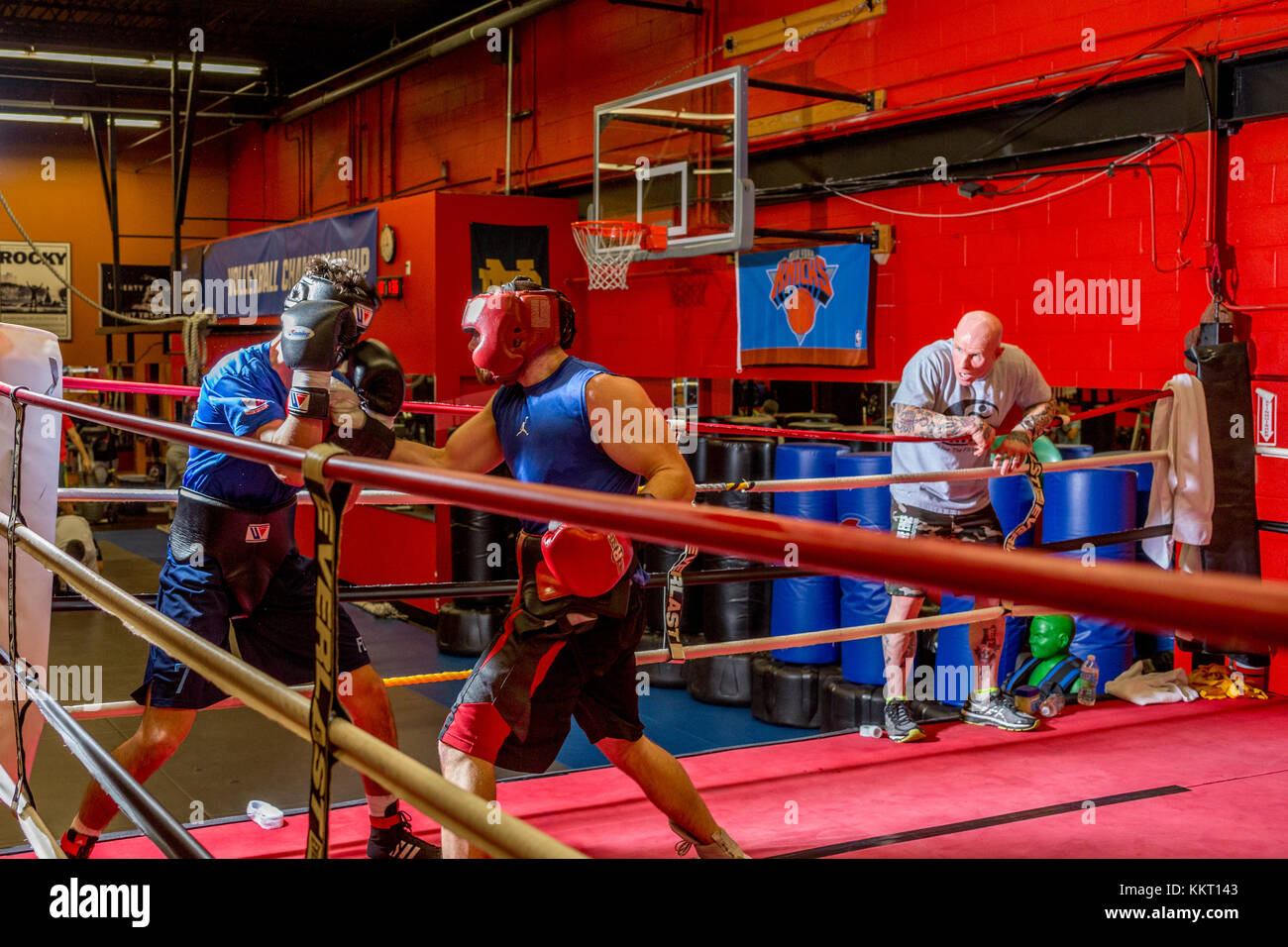 Amateur boxers wearing protective headgear sparring in a gym while their trainer looks on from