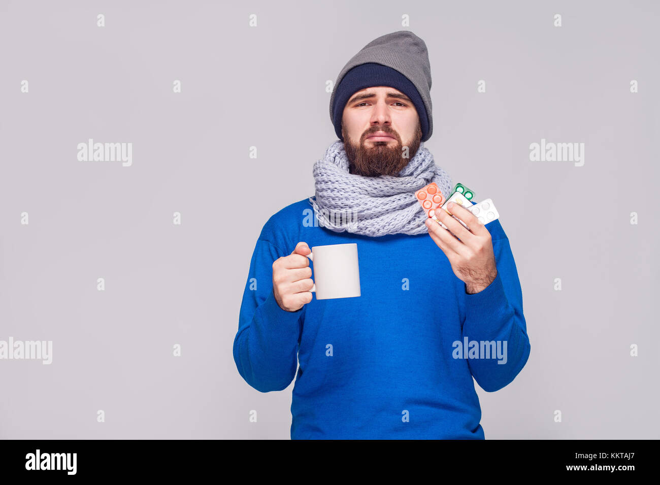 Sick bearded man holding cup with tea, many pills. Studio shot, isolated on gray background Stock Photo
