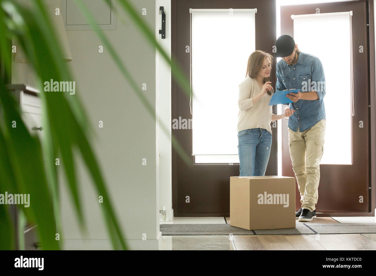Young woman receiving parcel cardboard box from courier at home Stock Photo