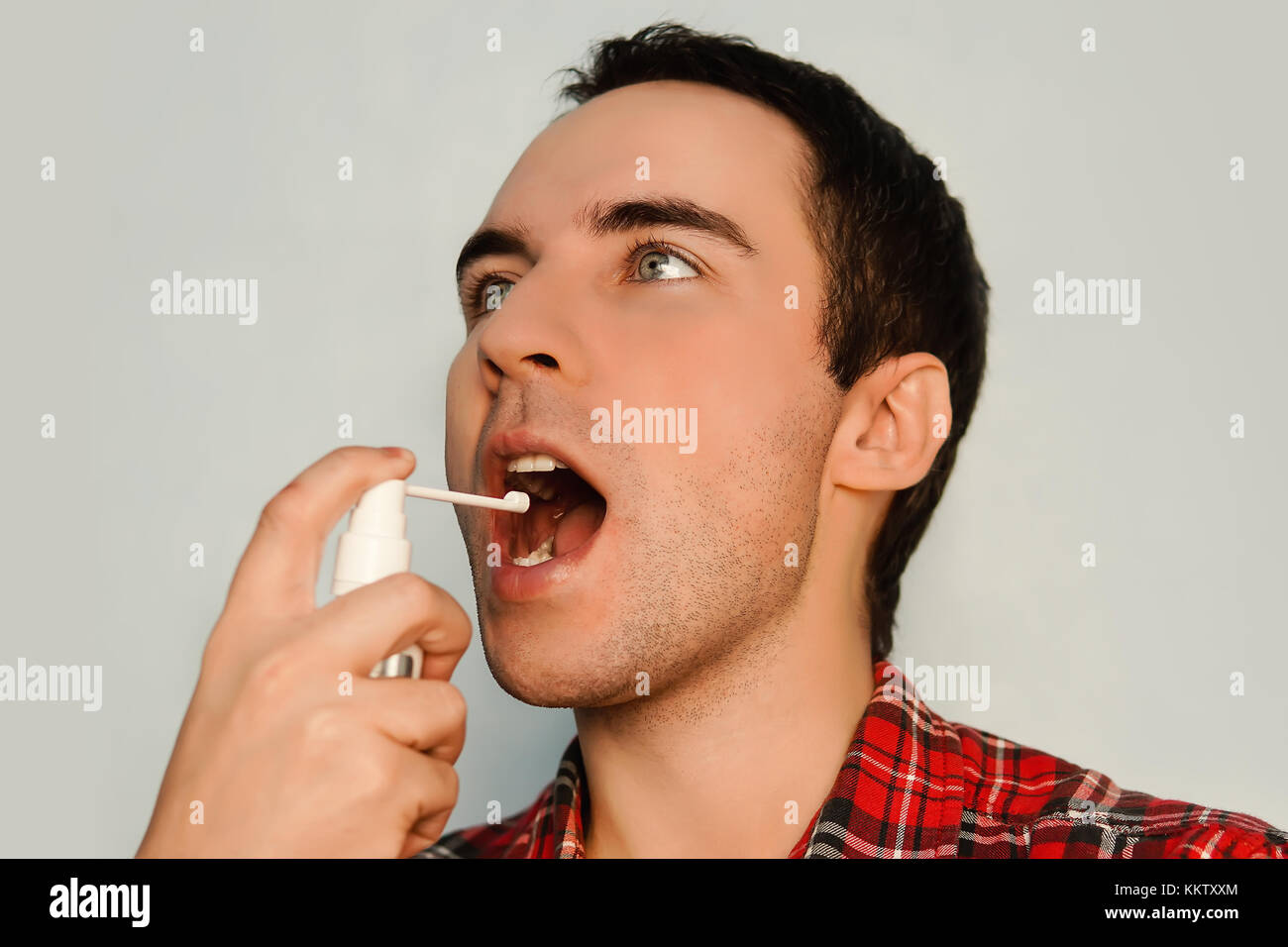 A young man between 30 and 20 years old dressed in a non formal manner has sore throat. Spray to improve your breath. The fight against foul breath. P Stock Photo