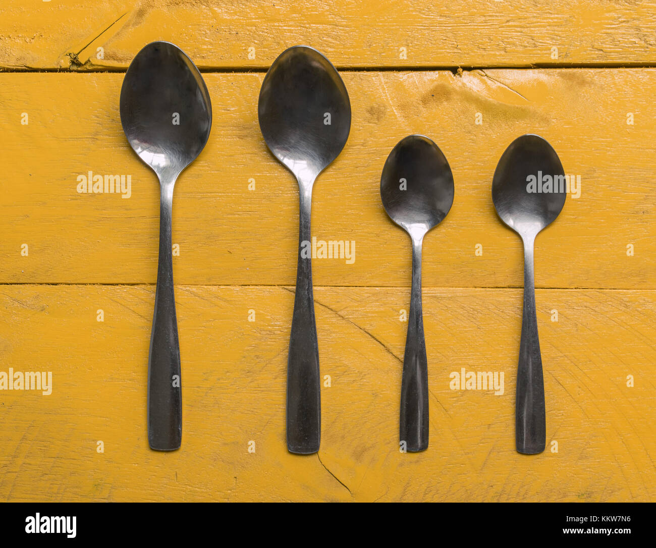 Set of four silver spoons on top of a yellow wooden surface background tabletop, aligned and organized Stock Photo