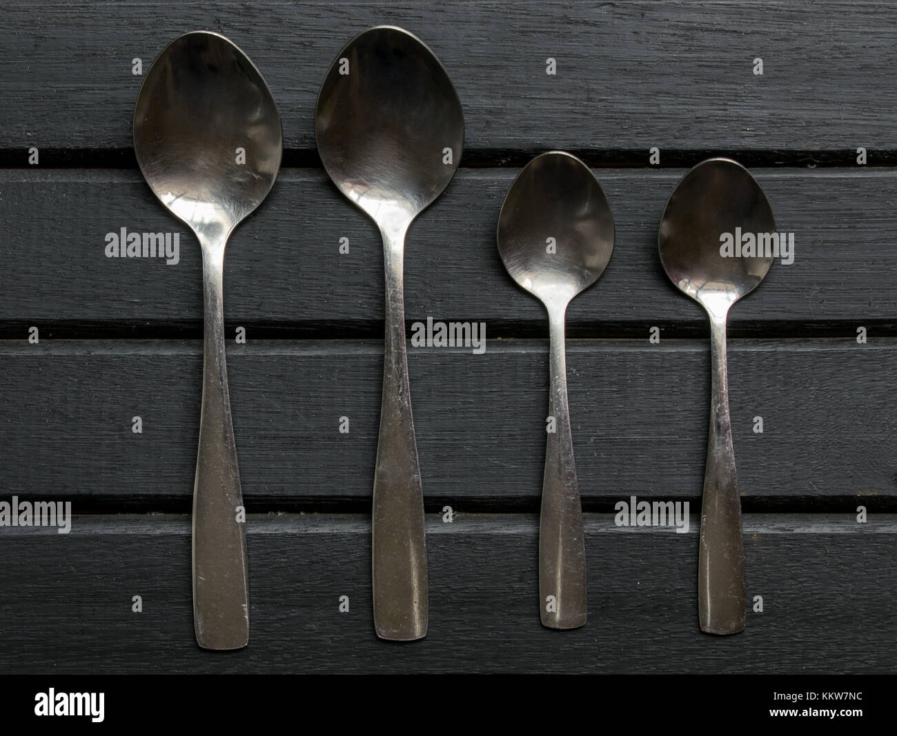 Set of four silver spoons on top of a black wooden surface background tabletop, aligned and organized Stock Photo