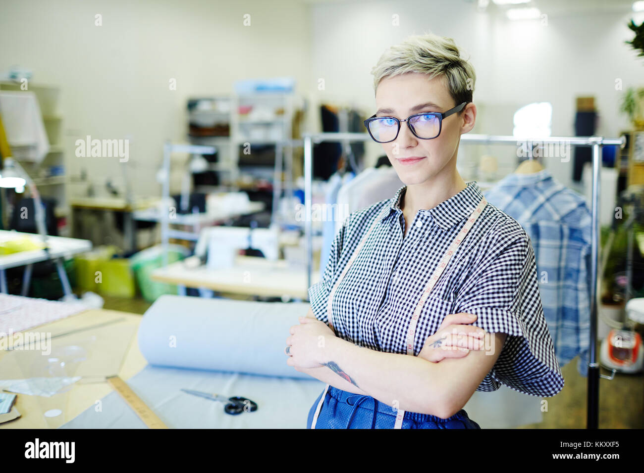 Modern seamstress in casualwear looking at camera by her workplace in