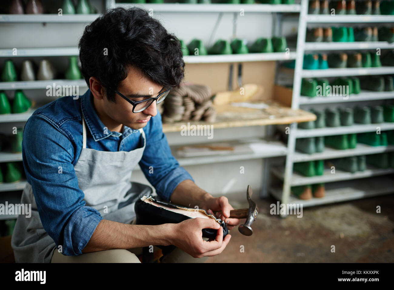 Professional shoemaker hammering nails into shoe sole through leather