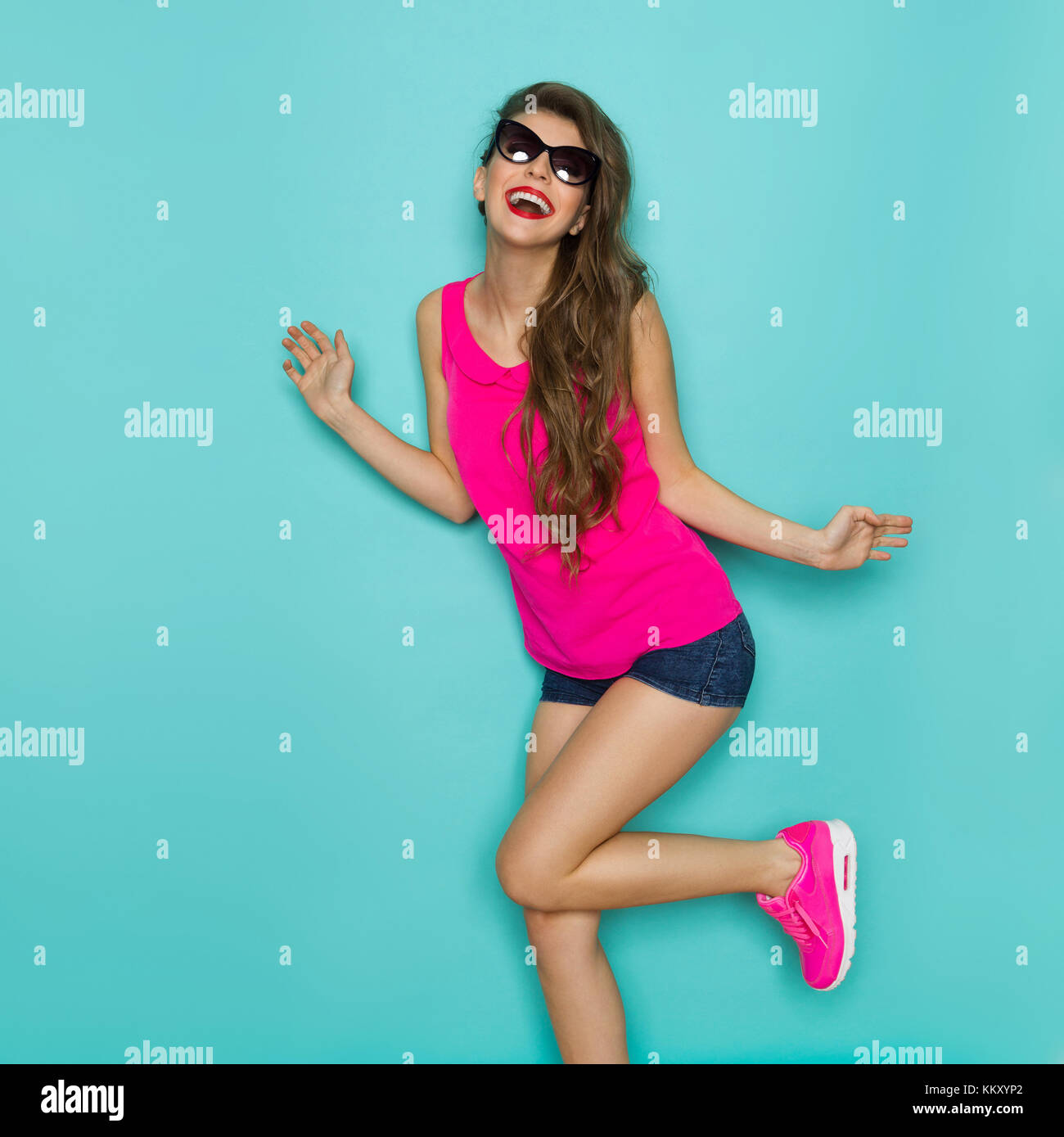 Beautiful girl in sunglasses, jeans shorts and pink top dancing with