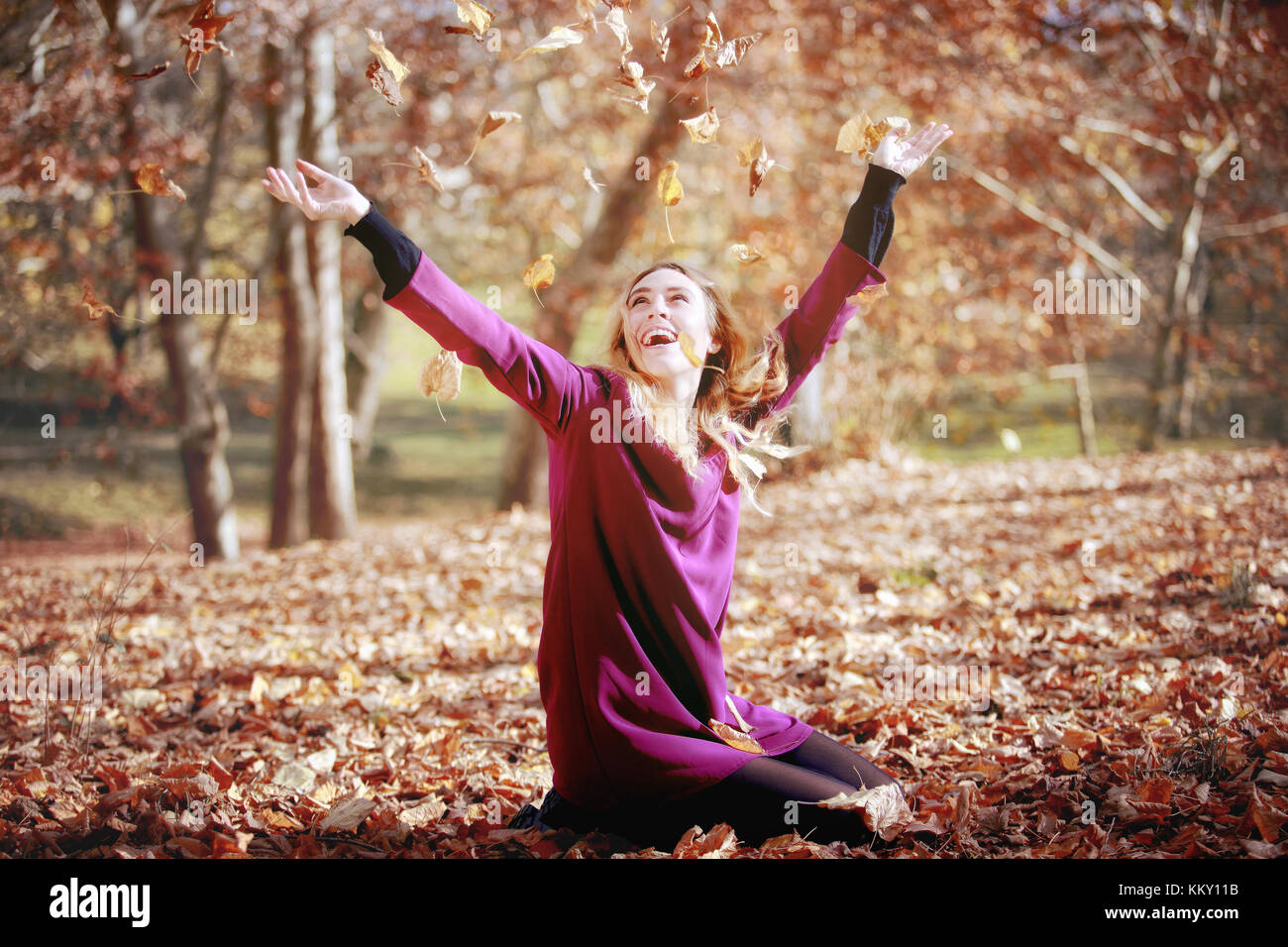 Young woman in beautiful autumn park, concept autumn. Girl, sitting in the woods, throws leaves in the air and smiles. Stock Photo