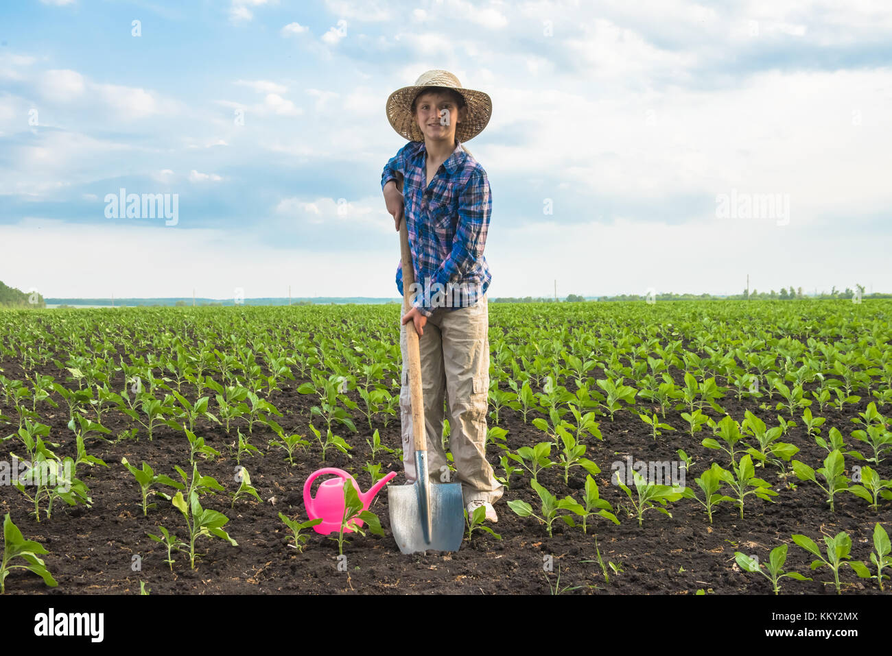 Happy small farmer with spade and watering can in spring field gardening Stock Photo