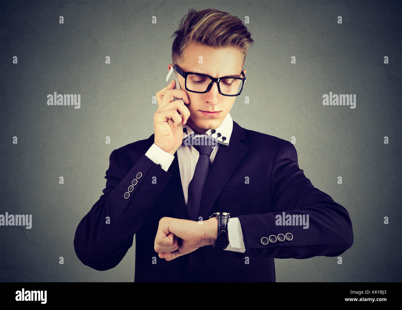 Business and time management concept. Businessman looking at wrist watch, talking on mobile phone. Stock Photo