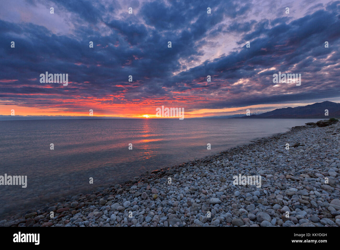 Sunrise and cloudscape at the pebble beach in Issyk Kul Lake, Kyrgyzstan. Stock Photo