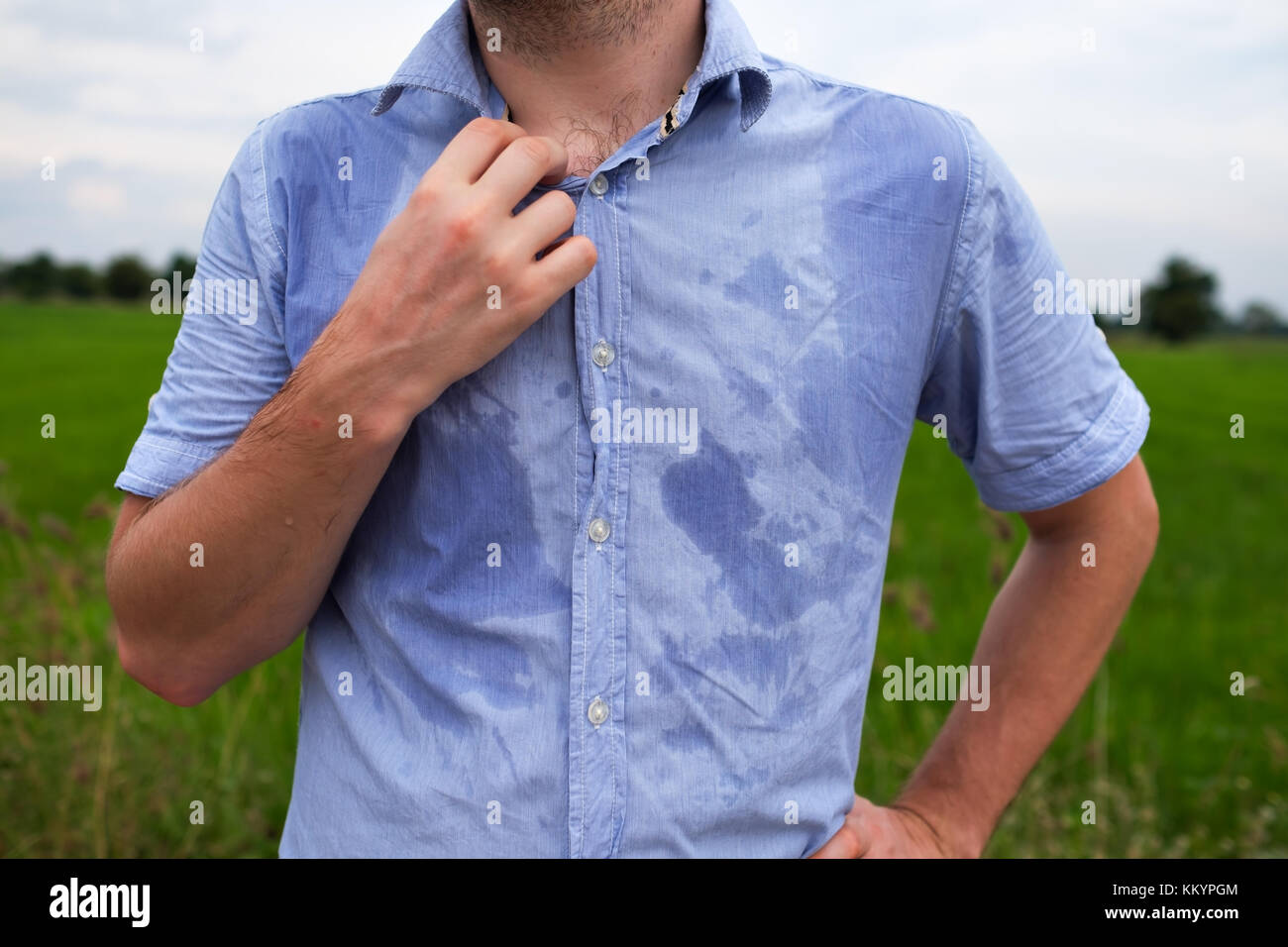 Man with hyperhidrosis sweating very badly under armpit in blue shirt, isolated on grey Stock Photo