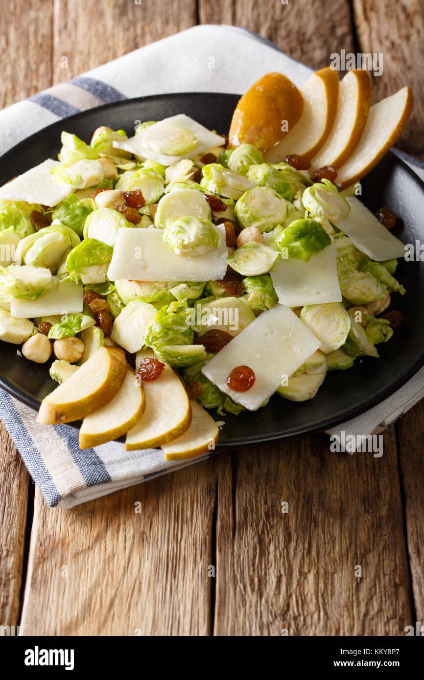 Tasty salad of shredded Brussels sprouts, hazelnuts, cheese, raisins and pears closeup on a plate. vertical Stock Photo