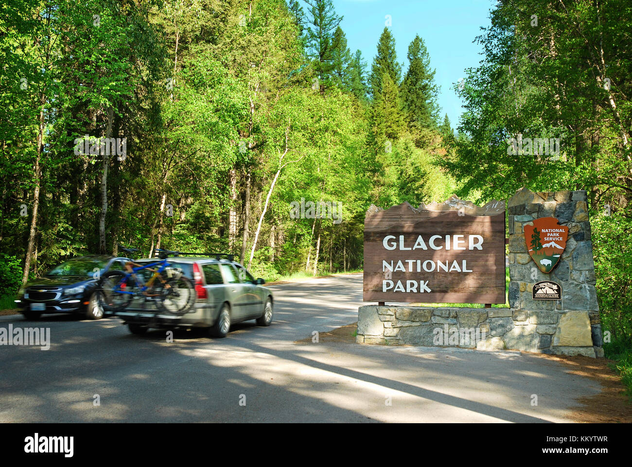 Two cars driving past the west entrance to Glacier National Park in Montana Stock Photo