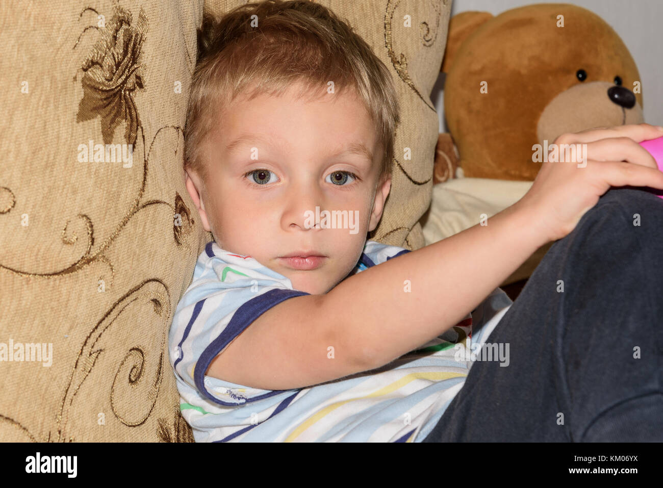 Portrait of fair-haired little boy playing with plasticine and bear home on the sofa Stock Photo