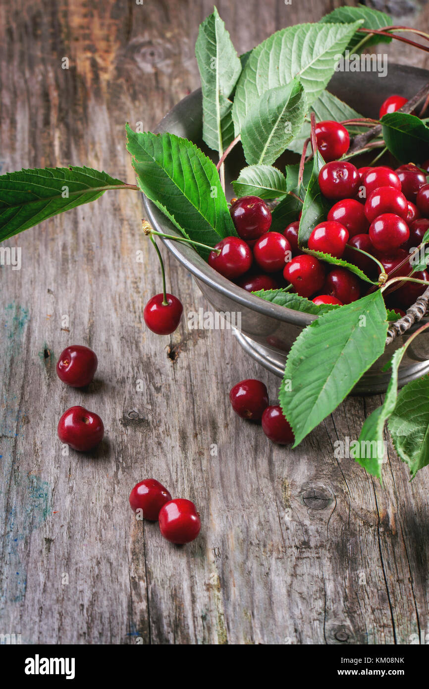 Metal bowl of fresh cherries with leaves on old wooden table Stock ...