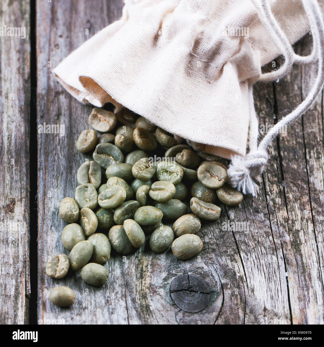 Sack with unroasted green coffee beans over wooden background. Square image with selective focus Stock Photo