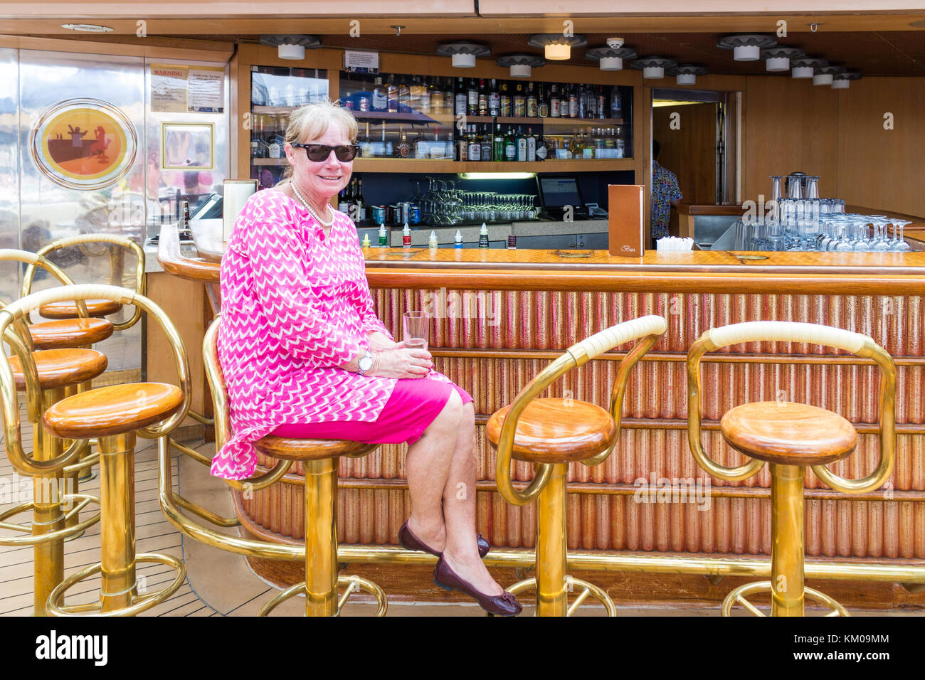 Senior woman with drink sat at bar on the Holland America line cruise ship Volendam Stock Photo