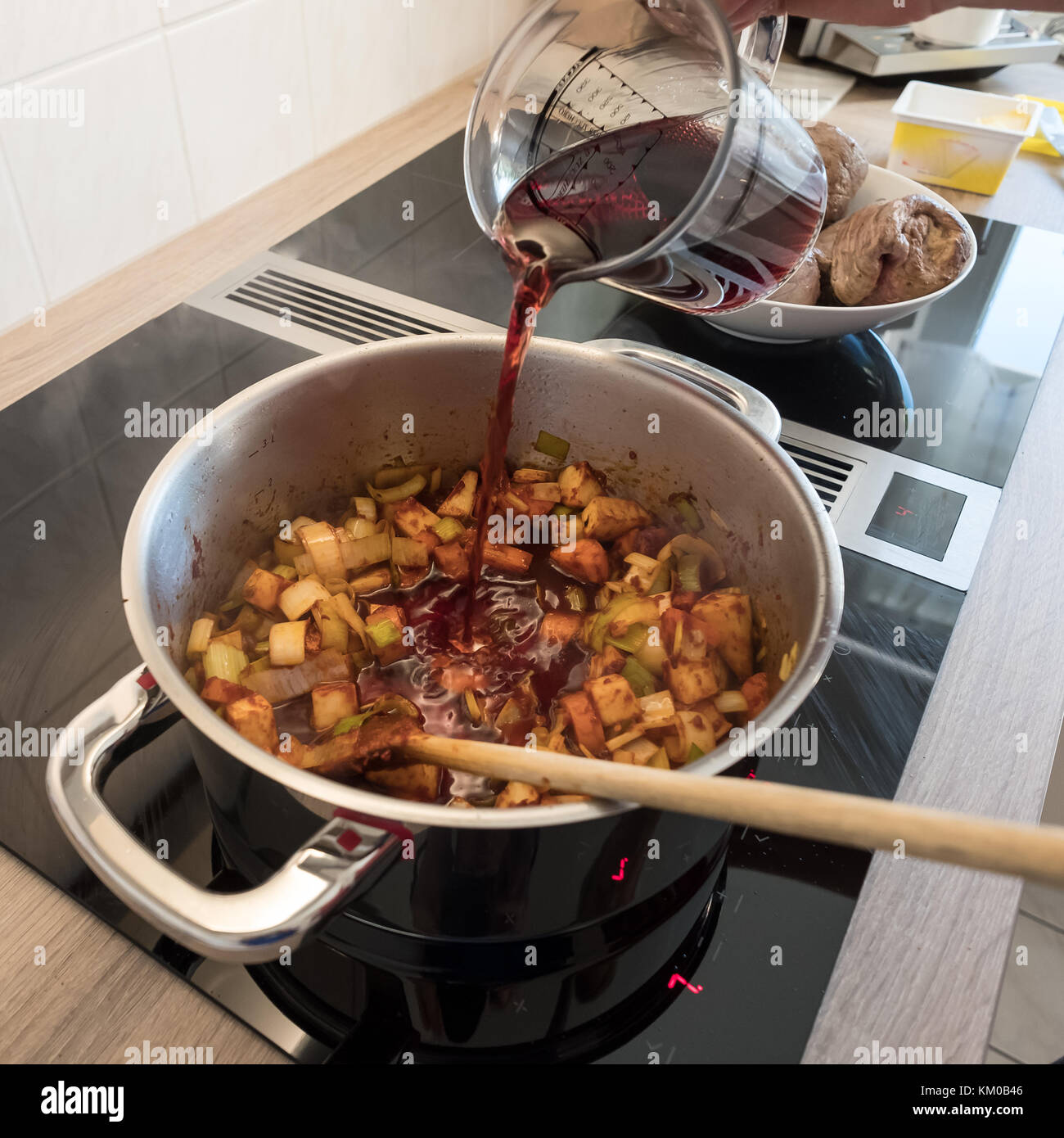 Female hand is pouring red wine into roasting vegetable to deglaze ...