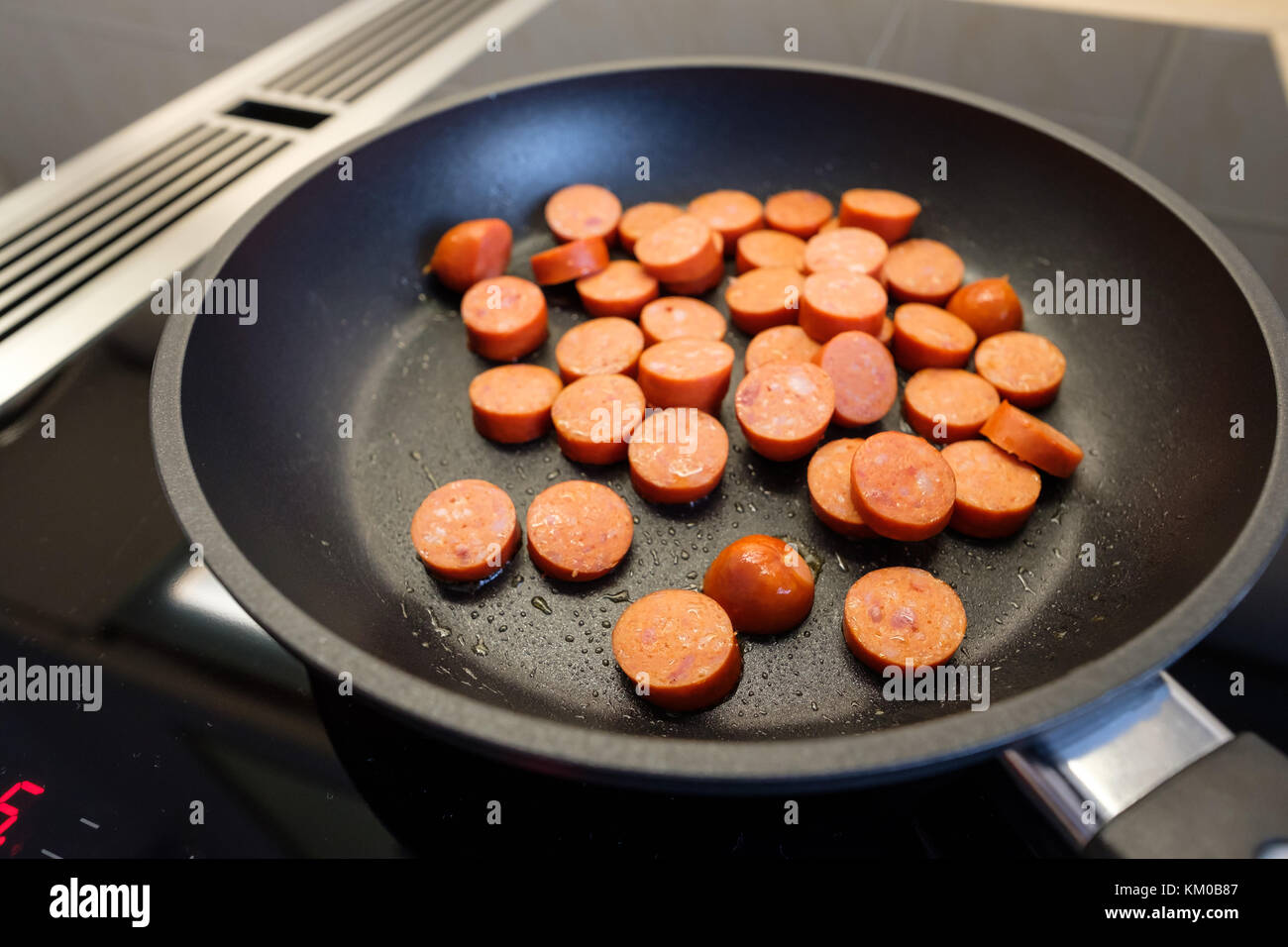 Debreziner sausage in a frying pan of a cooking hob with cooktop
