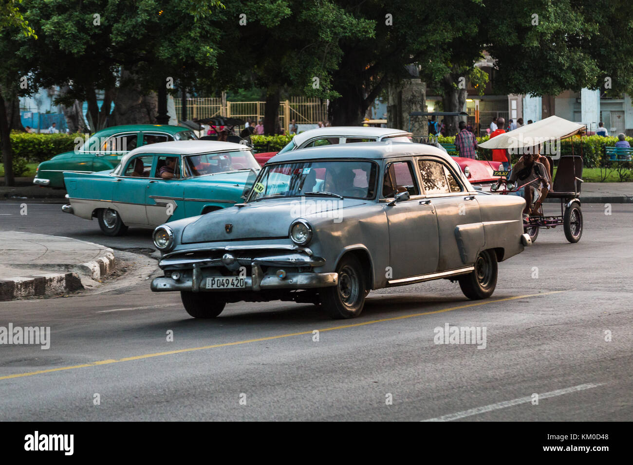 A bicitaxi and four American classical cars from the 1950s captured in a tight frame at sunset one August evening in 2014 on the streets of Havana. Stock Photo