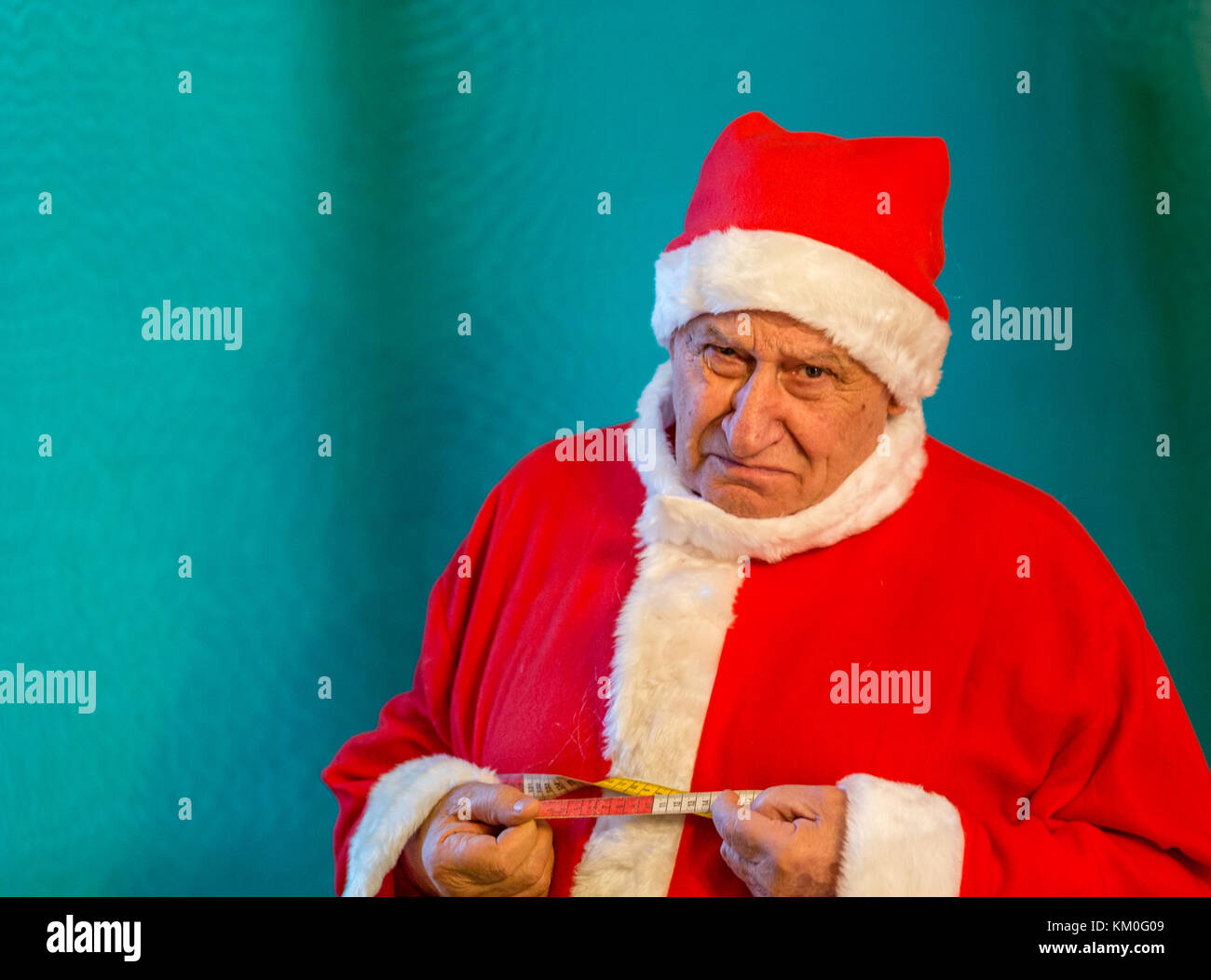 old man wearing Santa Claus costume  crying and measuring the circumference of his belly with a tape measure Stock Photo