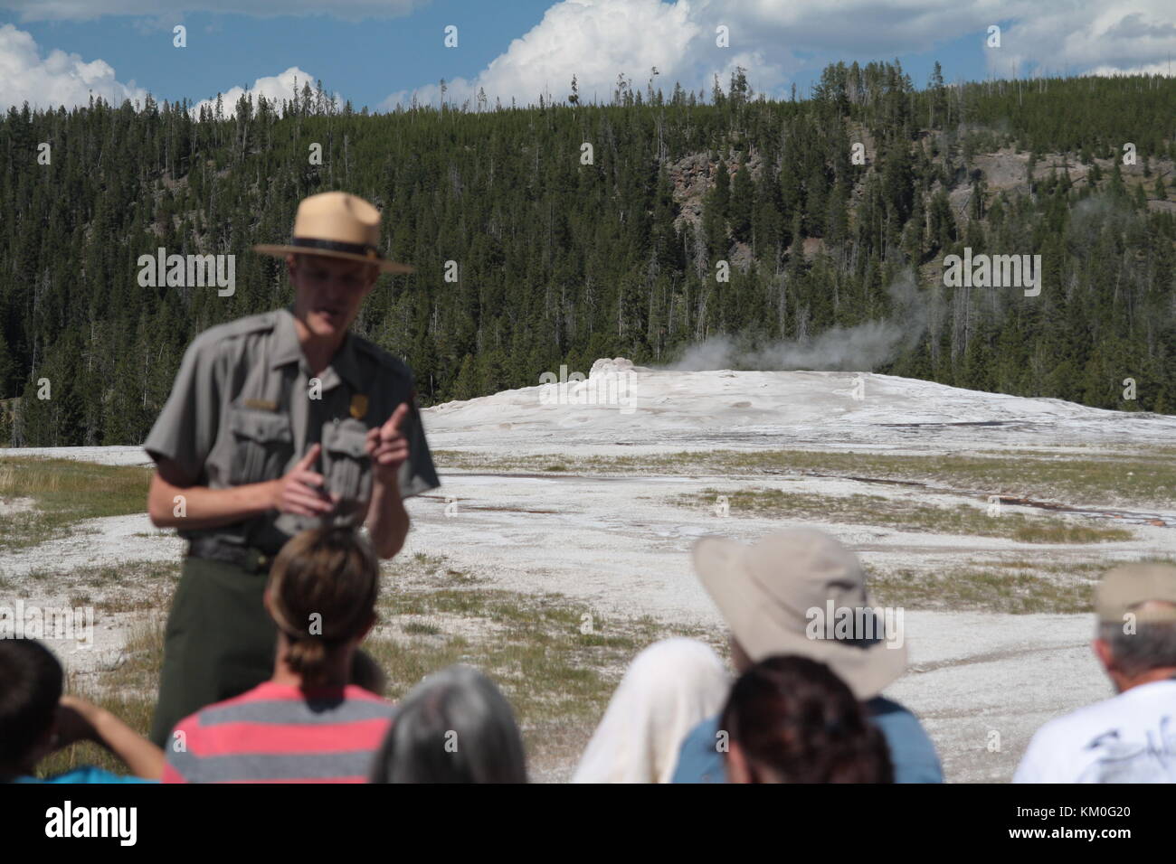 A Park Ranger In Uniform Explains To Visitors The Functioning Of The Famous Old Faithful Geyser