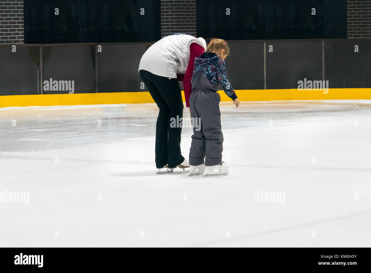 Happy family indoor ice skating at rink. Winter activities. Young girl instructor teaches a little girl to skate. Mother and daughter holding hands Stock Photo