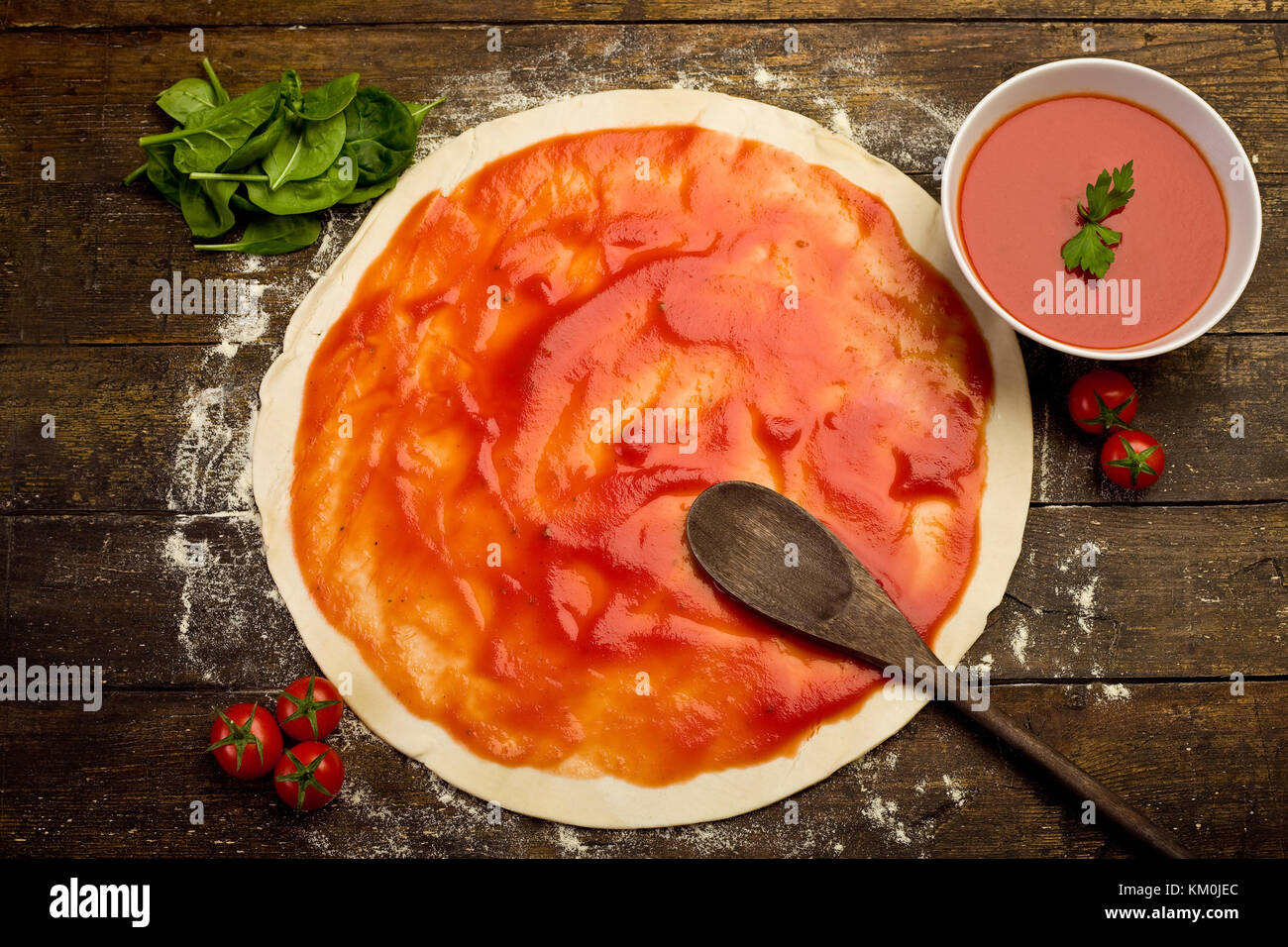 pizza dough with tomato sauce on rustical wooden table Stock Photo