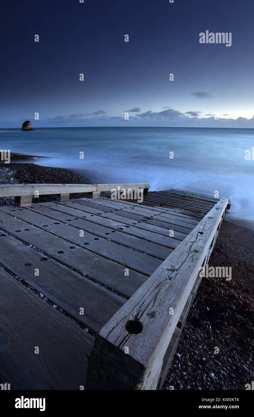 A beautiful and atmospheric seascape of a wooden slipway and misty sea going down the beach to the sea on a cold autumnal evening at sunset. Moody. Stock Photo