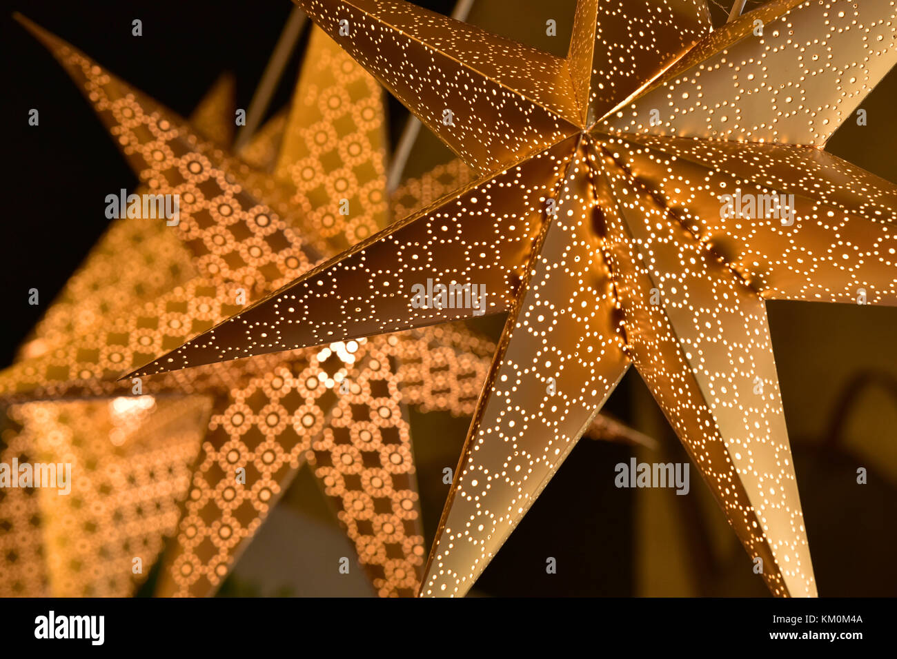 Golden coloured christmas star decorations illuminated to celebrate the festive season. Astral designs and glittery style of decor for xmas. Shining. Stock Photo