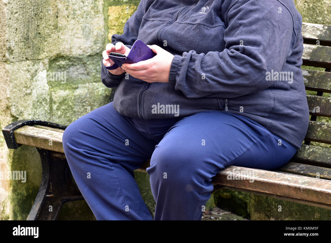A Fat Or Obese Person Sitting On A Bench Texting Or Messaging