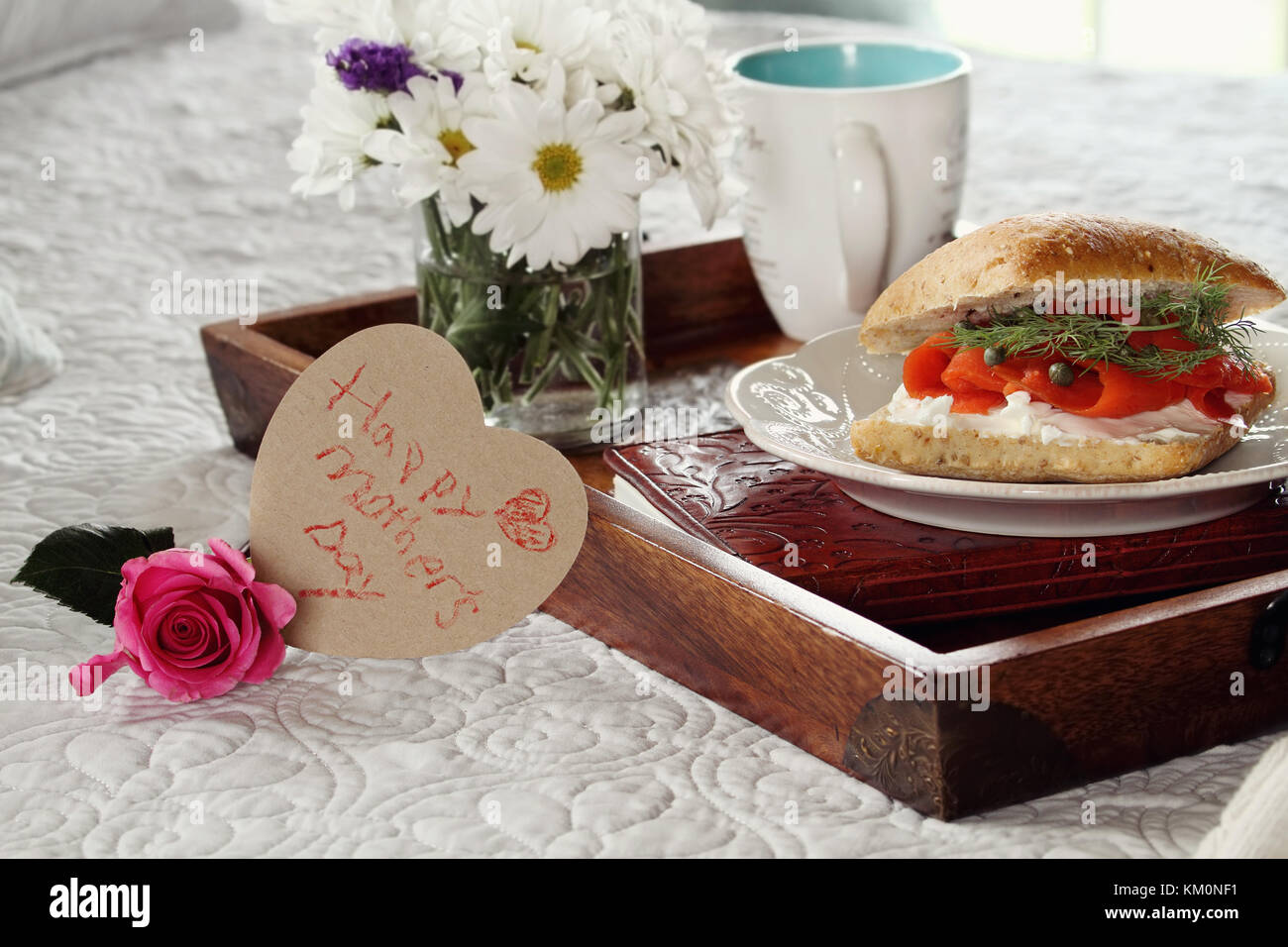 Child's handwritten message on heart shaped card and flowers with breakfast served in bed. Extreme shallow depth of field with selective focus on hear Stock Photo