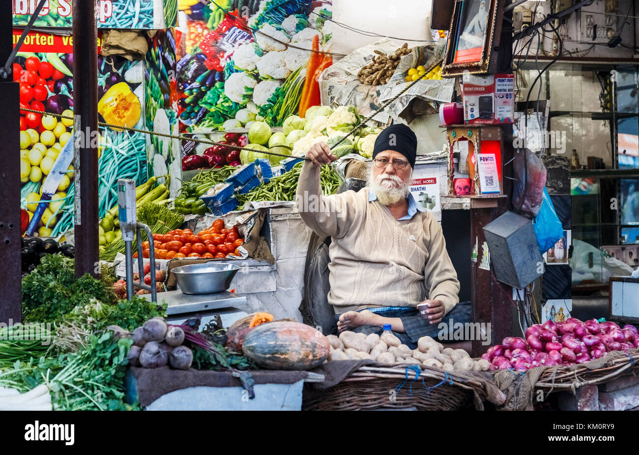 Local male Sikh stallholder sitting cross-legged in a vegetable shop, Amritsar, a city in north-western India in the Majha region of Punjab Stock Photo