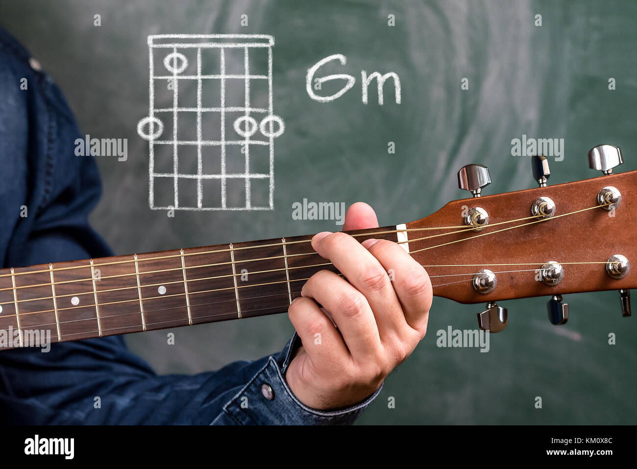 Man in a blue denim shirt playing guitar chords displayed on a blackboard,  Chord Gm Stock Photo - Alamy