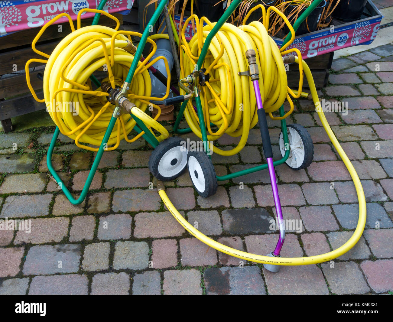 Two market garden hose reels with yellow kink resisting hose on portable reels and having spray nozzles convenient deployment in a garden centre Stock Photo